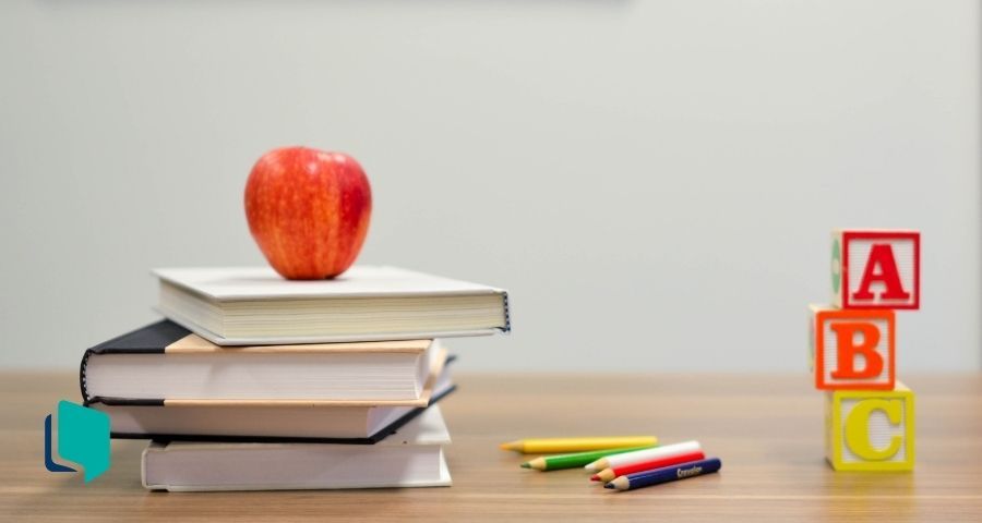 Livros sobre uma mesa com uma maçã em cima e lápis. Plano de aula de acordo com a BNCC.