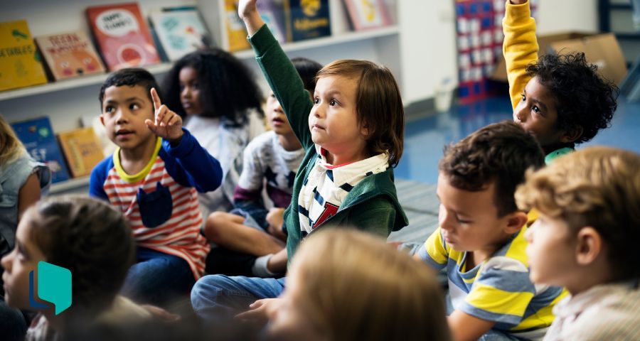 O que ensinar de inglês na educação infantil? Alunos crianças sentados no chão com a mão levantada