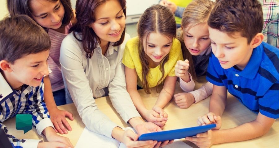 4 benefícios da Gamificação na Educação Infantil. Foto de uma Professora com alunos olhando para um tablet.
