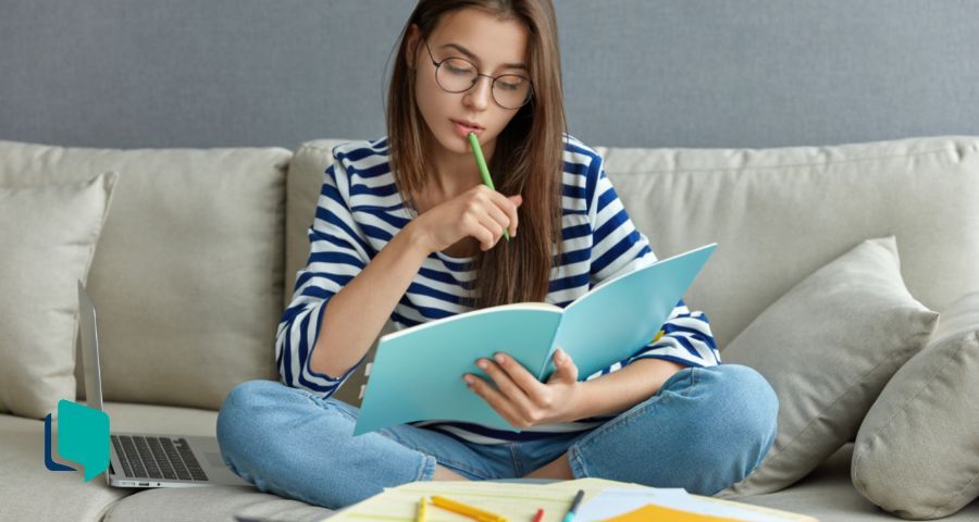 Atividades de inglês: na foto uma menina sentada no sofá estudando com caderno no colo e pc ao lado